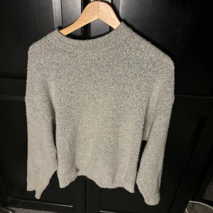 Ljusgrå stickad tröja - Mysig ljusgrå stickad tröja med rund halsringning och långa ärmar. Tröjan har en enkel och stilren design med ribbade muddar vid ärmslut och nederkant. Perfekt för lager-på-lager under kyliga dagar.