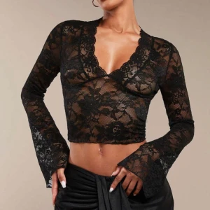 Svart spetsblus med v-ringning - Säljer en svart, transparent spetsblus med lång ärm och v-ringad hals. Blusen är croppad och har ett blommigt spetsmönster. Perfekt för att skapa en trendig och elegant look. Sitter jättefint på kroppen. Ej använd bara provats en gång. 