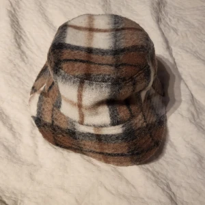 Primark Gingham Bucket Hat  - Säljer en snygg och knappt använd bucket hat från Primark i gingham mönster. Hatten har bruna, svarta, vita och beige rutor och är fodrad med vitt tyg på insidan. Perfekt accessoar för att lyfta din outfit.
