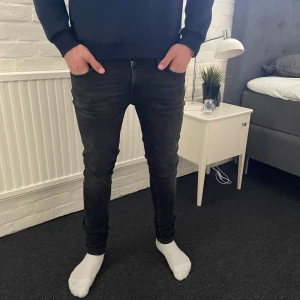 Nudie jeans skinny lin W31 L32 - Säljer ett par svarta jeans från Nudie Jeans med klassisk femficksdesign. Jeansen har smal passform och raka ben, tillverkade i stretchigt denimtyg för extra komfort. Perfekta för dig som gillar stilrena och tidlösa jeans.
