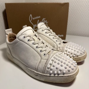 Vita sneakers med nitar från Christian Louboutin - Hej! Jag säljer riktig sköna Louboutin skor i vit färg och med nitar fram och skorlek 42-43!   Jag köpte dessa skor från en kompis och jag gjorde rent dom så jag har inte använt dom utan vill bara sälja vidare! Dom har Inga hål men sprickor lite back och sidorna, och två av nitar har gått av.   Skorna kommer i original förpackning och allt är med som på bilden!   Priset kan diskuteras!  Om du har frågor eller önskar flera bilder är det bara att höra av!