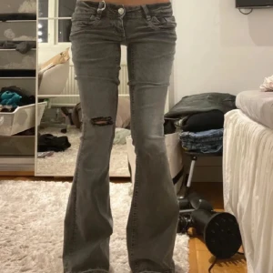 Grå bootcut jeans med slitning - Säljer ett par ljusgrå bootcut jeans med låg midja och slitning på ena benet. Midjemått :36cm Innerbenslängd:82cm första bilden lånad 