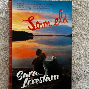 Bok ”Som eld” - En bok av Sara Lövestam som handlar om kärlek och vänskap under en sommar. Omslaget visar en solnedgång vid en sjö med två personer som sitter tillsammans. Perfekt för den som gillar romantiska berättelser med djup och känsla. Helt ny. 