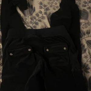 Mörk blåa byxor från Juicy Couture - Snygga svarta byxor från Juicy Couture med glittriga knappar på bakfickorna och snörning i midjan. Perfekta för en stilren look.