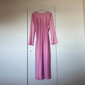 Rosa långklänning  - Elegant rosa långklänning med långa ärmar och en vacker detalj där bak där man kan knyta. Klänningen har en mjuk och glansig yta som ger en lyxig känsla. Den är helt ny så är i väldigt bra skick och lappen sitter fortfarande kvar. Den är i storlek L men skulle mer säga att den är om en M då materialet inte är så stretchigt🫧🤍💕