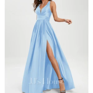 Ljusblå långklänning från JJ's House - Elegant ljusblå långklänning med v-ringning och smala axelband som korsas i ryggen. Klänningen har en hög slits framtill och ett fint fall som ger en vacker siluett. Perfekt för speciella tillfällen. Känningen är i marinblå färg, alltså inte färgen på bilden. Skickar egna bilder vid intresse. Orginalpris 1200