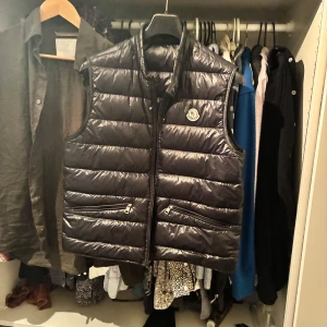 Svart dunväst från Moncler - Snygg svart dunväst från Moncler med dragkedja och två fickor framtill. Perfekt för lager-på-lager under kyligare dagar. Klassisk design med Moncler-logga på bröstet.