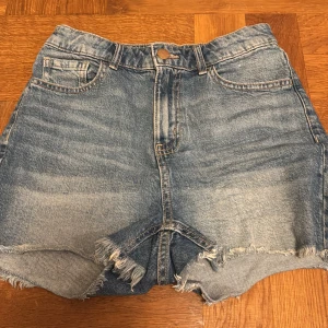 Jeansshorts  - Snygga jeansshorts från Lindex med fransiga kanter och klassisk femficksdesign. Perfekta för en avslappnad sommarlook. De har en knapp och dragkedja framtill.