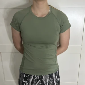 Olivgrön träningstopp - Snygg olivgrön träningstopp med korta ärmar och en tight passform. Perfekt för gymmet eller löprundan. Tillverkad i ett mjukt och stretchigt material som andas.