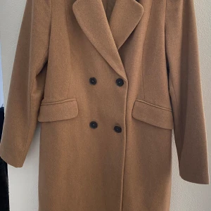 Brun beige kappa från ONLY - Säljer en stilren brun kappa från ONLY i storlek L. Kappan har en klassisk design med dubbelknäppning och långa ärmar. Perfekt för höst och vinter.
