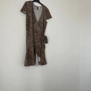 Leopardmönstrad omlottklänning - Trendig leopardmönstrad omlottklänning med korta ärmar och knytning i midjan. Perfekt för en djärv look.