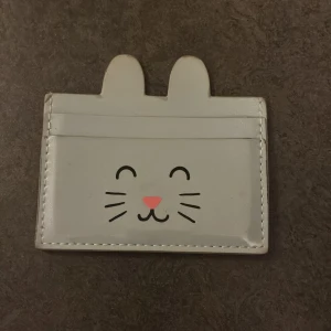 Söt korthållare med kattmotiv - Liten plånbok med ett gulligt kattansikte och öron på framsidan. Perfekt för att hålla ordning på kort. Den är ljusblå med rosa och svarta detaljer.