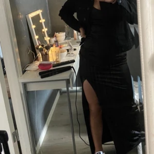 Svart långklänning med spetsdetaljer - Elegant svart långklänning med smala axelband och v-ringad spetsdetalj. Klänningen har en slits på sidan för en stilfull look. Perfekt för festliga tillfällen. Inköpt för 800kr