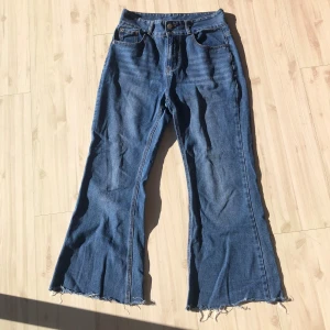 Blå flarejeans  - Säljer ett par blå jeans med fransiga kanter och en bootcut-stil. De har en klassisk femficksdesign och knäppning med dragkedja. Perfekta för en avslappnad look.