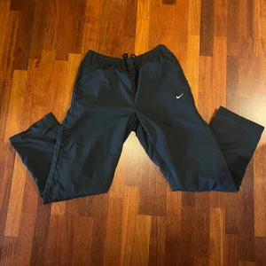 Svarta vintage träningsbyxor från Nike - Säljer ett par svarta relaxed vintage träningsbyxor från Nike med elastisk midja och dragsko. Byxorna har en liten vit Nike-logga på ena benet. Stilen är mest Y2k och streetwear. Storleken är L men skulle säga att den passar de flesta mellan 175 - 185 cm. De är vintage och därav svåra att få tag på men trots detta i nästan nyskick. 