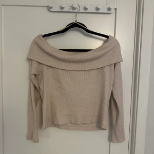 Beige offshoulder tröja - Säljer en stilren beige offshoulder tröja med ribbad struktur. Tröjan har långa ärmar och en bred krage som ger en elegant look. Perfekt för en avslappnad men chic stil.
