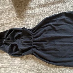 Svart klänning från Darja - Mini-klänning med fint fall i fram och öppen rygg. Mycket fint skick. Köpt från Isabel Adrians Sellpy-shop. Finns ingen storleks märkning men passar 32-34