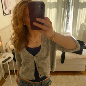 Grå kofta med knappar - Säljer en mysig grå kofta med knappar framtill. Koftan har trekvartsärmar, perfekt för lager-på-lager-stil. Den är tillverkad i ett mjukt material som ger en avslappnad look.