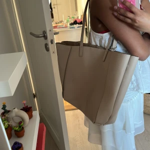 Beige axelväska - Snygg beige axelväska med rymligt inre och praktiska fack. Väskan har en dragkedja och knäppning för extra säkerhet. Perfekt för att bära med sig allt man behöver under dagen.