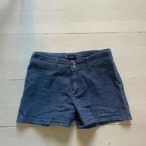 Blå jeansshorts från Filippa K - Snygga blå jeansshorts från Filippa K med två knappar fram. Perfekta för sommardagar och har en klassisk design som aldrig går ur stil. De är bekväma och lätta att matcha med olika toppar. Storleken är M men skulle säga S