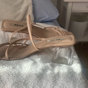 Beige sandaler från NA-KD - Snygga beige sandaler från NA-KD med transparent klack och tunna remmar. Perfekta för en stilren look.