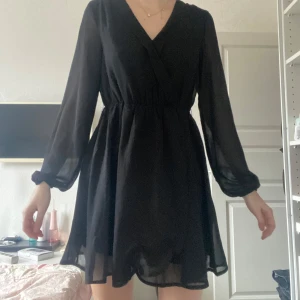 Svart långärmad klänning - Snygg svart klänning från NLY TRENDmed långärmad design och omlott framtill. Perfekt för en stilren look med sin korta längd och lätta material.