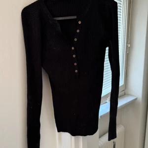 Svart ribbad långärmad tröja - Snygg svart ribbad tröja med långa ärmar och knappar framtill. Perfekt för en stilren look och passar bra till både jeans och kjol.