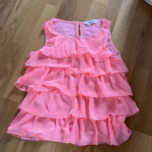 Rosa volangtopp från H&M - Säljer en söt rosa volangtopp från H&M. Toppen är ärmlös och har flera lager av volanger som ger en lekfull look. Perfekt för sommarens varma dagar! 💖