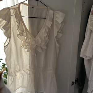 Vit blus med volangdetaljer - Säljer en elegant vit blus med volangdetaljer och v-ringning. . Blusen har korta ärmar och ett lätt och luftigt material🥰🥰 Blusen är köpt på Zara men har ingen lapp