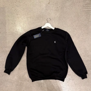 Svart tröja från Polo Ralph Lauren - Säljer en stilren svart jumper från Polo Ralph Lauren med deras ikoniska logga broderad på bröstet. Tröjan har långa ärmar och en klassisk rund halsringning. Perfekt för en avslappnad och snygg look. Storlek M 