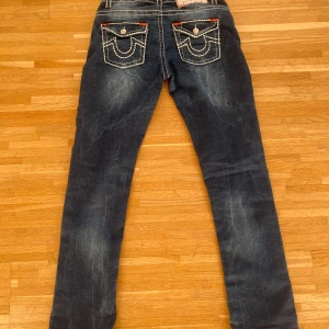 Mörkblå jeans från True Religion - Snygga mörkblå jeans från True Religion med tydliga vita sömmar och orange detaljer. Byxorna har en klassisk femficksdesign och knappar.