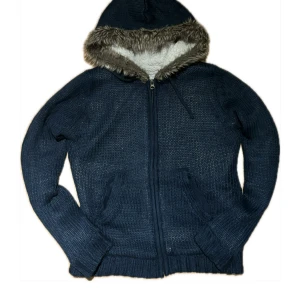 fodrad tröja - Säljer en mörkblå stickad jacka med huva och dragkedja. Jackan har ett mjukt foder och en kant av pälsimitation runt huvan. Storlek S.