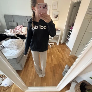 Svart hoodie från Adidas - Säljer en svart hoodie från Adidas med dragkedja och stor logga på framsidan. Tröjan har en luva och långa ärmar, perfekt för en avslappnad stil. Passar bra till både jeans och träningsbyxor.