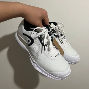 Vita tennisskor från Head - Snygga vita tennisskor från Head med svarta detaljer och snörning. Perfekta för tennisbanan med en slitstark sula och bekväm passform. Skorna har en modern design och är idealiska för både träning och match. Helt nya med tags 🏷️ 