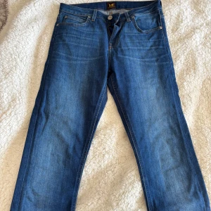 Blå jeans från Lee - Snygga blå jeans från Lee med klassisk femficksdesign och knappgylf. Perfekta för en avslappnad stil. Märkeslogga på bakfickan och bälteshällor för extra stilpoäng.