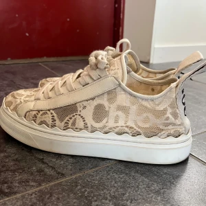Beige sneakers från Chloé - Snygga beige sneakers från Chloé med spetsdetaljer och snörning. Skorna har en rund tå och en vit sula. Perfekta för en stilren look med en touch av elegans. Nypris 5700kr, använda men i fint skick 