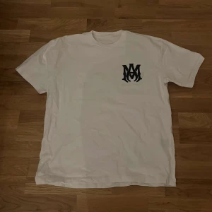 Amiri t shirt  - Säljer en stilren vit t-shirt från Amiri med ett svart tryck på bröstet och stort Amiri-tryck på ryggen. Perfekt för en avslappnad look. Passar bra till jeans eller shorts.
