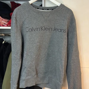 Grå sweatshirt från Calvin Klein Jeans - Säljer en stilren grå sweatshirt från Calvin Klein Jeans. Tröjan har en rund halsringning och långa ärmar. Perfekt för en avslappnad look.