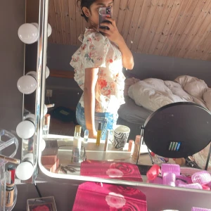 Blommig blus med volangdetaljer - Säljer en söt blommig blus med volangdetaljer. Blusen har korta ärmar och ett luftigt snitt, perfekt för varmare dagar. Den har ett vackert blommönster i ljusa färger som ger en romantisk känsla.