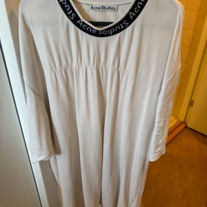 Acne Studios T-Shirt - Säljer en stilren vit långärmad tröja från Acne Studios. Tröjan har en rund halsringning med Acne Studios-logga runt kragen. Perfekt för en avslappnad look. Har tråd som lossnat på botten av tröjan därav priset (se bild)