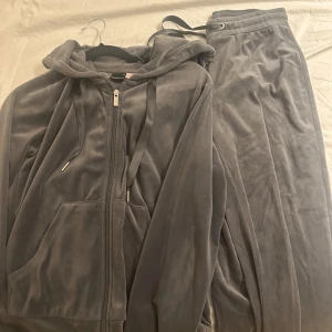 Grå mjukisbyxor och hoodie från Gina Tricot - Mysigt set med grå mjukisbyxor och matchande hoodie från Gina Tricot. Byxorna har resår och dragsko i midjan, och hoodien har dragkedja och fickor framtill. Perfekt för chill dagar eller när du vill vara extra bekväm. Byxorna är XS och koftan är S.