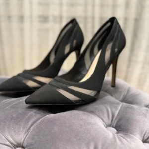 Svarta pumps med meshdetaljer från ALDO - Säljer ett par eleganta svarta pumps från ALDO med spetsig tå och höga klackar. Skorna har stilrena meshdetaljer på sidorna som ger en modern touch. Perfekta för dig som vill ha en klassisk men trendig look.