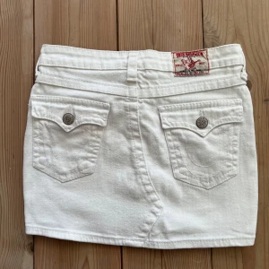 Vit jeanskjol från True Religion - Säljer en vit jeanskjol från True Religion med klassiska fickor fram och bak samt snygga silverfärgade knappar med logga. Kjolen har en låg midja och inga fläckar eller andra defekter! Nypris ligger runt 1000💕