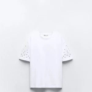 Vit t-shirt med pärldetaljer från Zara - Säljer en vit t-shirt från Zara med korta ärmar och snygga pärldetaljer på ärmarna. Perfekt för dig som vill ha en basic t-shirt med lite extra stil. Superenkel att matcha med jeans eller kjol!