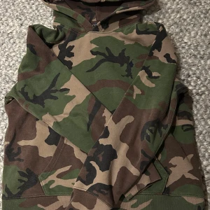 Camo hoodie från Polo Ralph Lauren - Säljer en camouflagemönstrad hoodie från Polo Ralph Lauren i storlek L i barnstorlek. Tröjan har huva, känguruficka och klassisk broderad logga på bröstet. Perfekt för dig som gillar streetwear och vill sticka ut med en snygg camo-look.