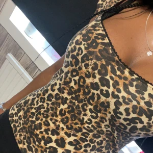 Leopardmönstrad topp från Nelly - Säljer en snygg leopardmönstrad topp från Nelly med v-ringning och svarta spetsdetaljer längs kanten. Toppen har korta ärmar och är tillverkad i ett mjukt, stretchigt material som sitter tight mot kroppen. Glamor topp🐆