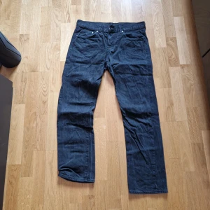 Svarta straight jeans från H&M - Säljer ett par svarta jeans från H&M i straight fit med regular midja. Klassisk femficksmodell i denim med knapp och dragkedja framtill. Perfekta för dig som gillar en enkel och tidlös stil.