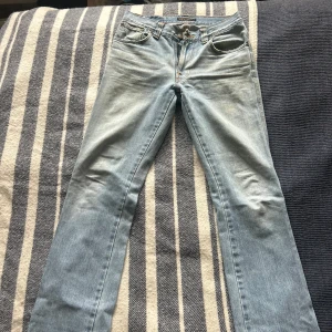 Ljusblå raka jeans från Nudie Jeans - Säljer ett par klassiska ljusblå jeans från Nudie Jeans med raka ben och femficksdesign. Jeansen har orangea sömmar och subtila broderier på bakfickorna. Perfekta för en avslappnad stil. Jeansen är lite mer lose i hur det sitter är vanligt och det korvar sig perfekt vid foten. Kan gå ner lite pris vid en snabb och bra affär.