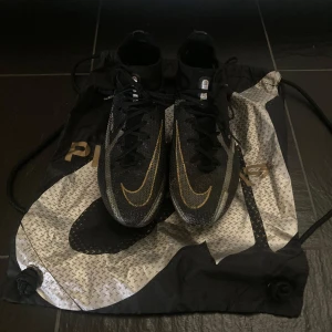Nike Phantom GX Elite fotbollsskor - Säljer ett par Nike Phantom GX fotbollsskor i svart med guldiga detaljer och snörning. Skorna har en strumpliknande passform och är designade för optimal bollkontroll på planen. Snygg design med tydlig Phantom-logga på sidan. Priset kan diskuteras🤙🏻