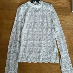Vit spetsblus från Vintage Stories - Säljer en romantisk vit spetsblus från Vintage Stories i storlek 36. Blusen har lång ärm, hög hals och vackert blommigt spetsmönster. Perfekt för dig som vill ha en feminin och elegant look med fina detaljer.